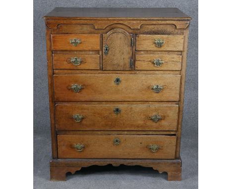 A Georgian country oak chest of drawers with shaped frieze and apron and an arrangement of cupboards and drawers on bracket f