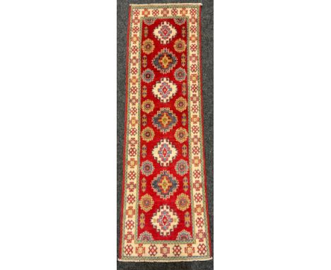 A Kazak small runner carpet / rug, multiple medallions within a field of light red, enclosed within a margin of stylised moti