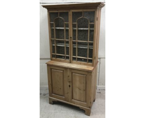 A 19th Century pine cabinet, the moulded cornice over two glazed doors enclosing two shelves, on a base of two fielded panell