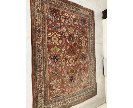 A large Persian carpet, the central panel set with all over scrolling foliate decoration on a red ground, within a stepped re
