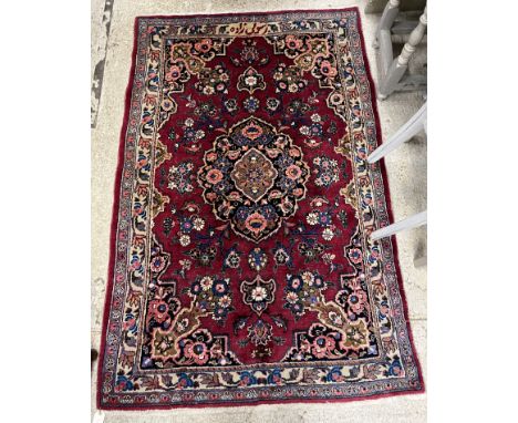 A Persian style carpet, the central panel set with floral decorated medallion on a plum ground within a stepped scrolling fol