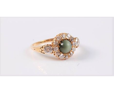 An 18ct cats eye chrysoberyl and diamond cluster ring, the central cats eye chrysoberyl cabochon, approx. 4.8mm diameter, sur
