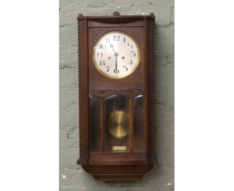 An oak cased 8 day wall clock chiming on a gong with Arabic numeral markers, key and pendulum.