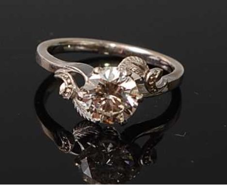 A white metal diamond solitaire ring, featuring a round brilliant cut diamond in a claw setting, with crossover leaf and scro