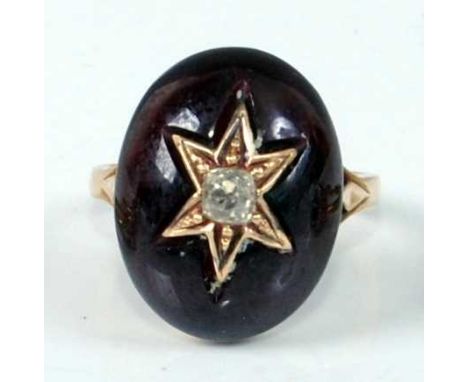 A yellow metal oval garnet mourning ring, featuring an oval cabochon cut garnet with centre six-ray star set with an old mine