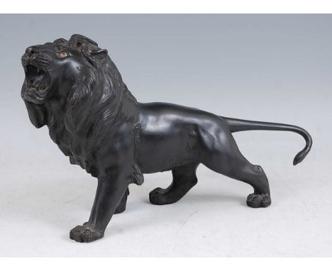 A Japanese Meiji period (1868-1912) bronze lion, modelled in striding roaring pose, with original glass eyes, the tail curled