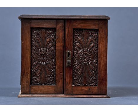 AN OAK SMOKER'S CABINET, EARLY 20TH C, ENCLOSED BY A PAIR OF ROSETTE AND LEAF SCROLL CARVED DOORS, THE INTERIOR WITH ONE LONG