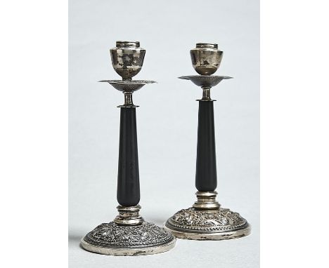 A PAIR OF SOUTH EAST ASIAN SILVER REPOUSSE CANDLESTICKS, C1900 AND LATER, WITH EBONISED WOOD PILLAR, THE FOOT CHASED WITH DRA