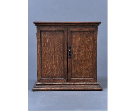 AN OAK SMOKER'S CABINET, C1920, ENCLOSED BY A PAIR OF PANELLED DOORS, THE INTERIOR WITH OPEN SHELVES, THE UPPER SHELF FITTED 