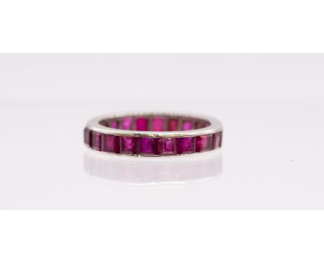 A ruby and white gold eternity band, comprising a row of calibre cut channel set rubies, each approx 3mm, width approx 4mm, s