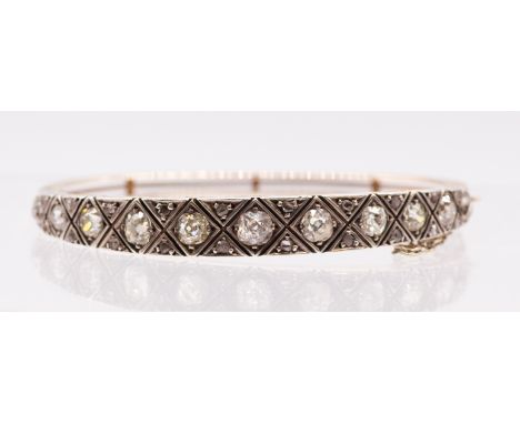 An Edwardian diamond and gold hinged bangle, comprising a platinum set with eleven graduated old cushion cut diamonds, set in