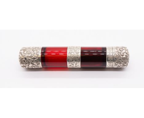 A late 19th Century white metal mounted plain ruby glass double ended scent bottle, the covers profusely chased with flowers,