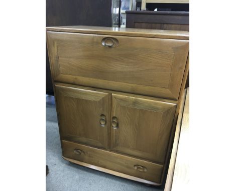 A Ercol cabinet with fall front a pair of cupboards doors and drawer Under.