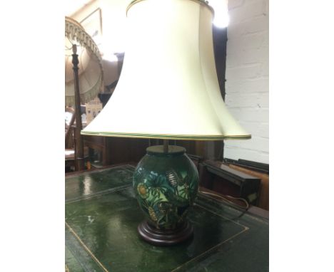 A Moorcroft table lamp with floral and pine cone decoratIon on a green ground, approx height with shade 62cm. Shipping catego