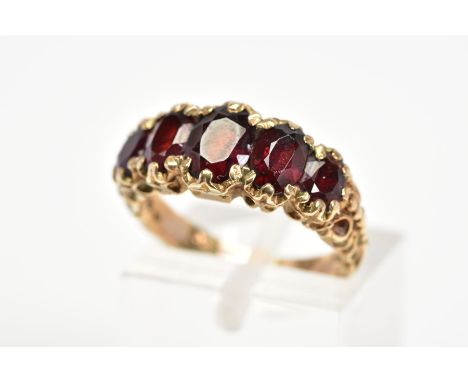 A 9CT GOLD RED GLASS RING, designed as five graduated oval cut red pastes within claw settings to the textured shoulders, wit