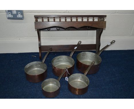 A SET OF FIVE COPPER GRADUATING PANS, with iron hooped handles and an oak hanging shelf