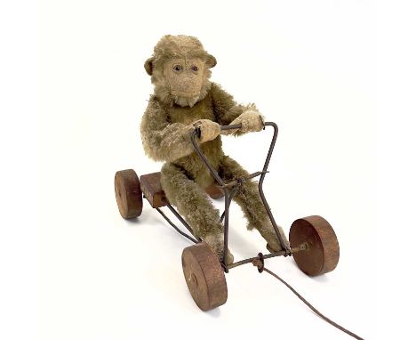 A 1930s plush monkey on a cart probably Steiff. With wrought iron frame and wood seat and wheels, length 29cm.