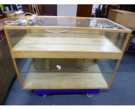 A LIGHT OAK GLAZED SHOP STYLE ILLUMINATED DISPLAY CABINET/COUNTER, the upper area with drop down access, the lower area with 