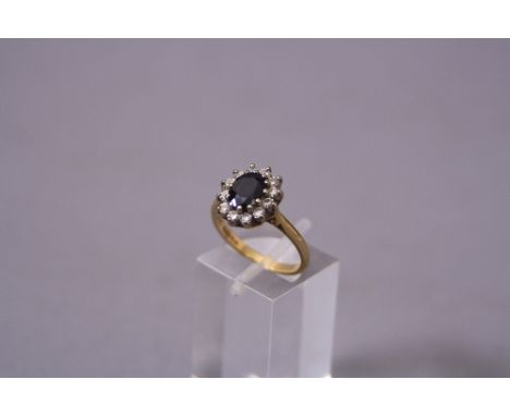 A LATE 20TH CENTURY 18CT GOLD SAPPHIRE AND DIAMOND OVAL CLUSTER RING, oval mixed cut dark blue sapphire measuring approximate