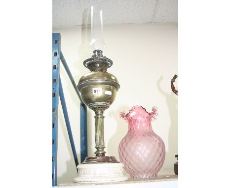 A LATE VICTORIAN BRASS BASED OIL LAMP, cranberry glass shade, white glazed circular ceramic base, with chimney