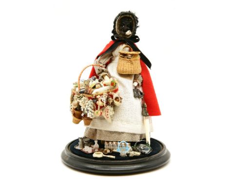 A black pedlar doll under glass dome, smoking a pipe, with a selection of trinkets, including comb, parasol, and a leg pipe t