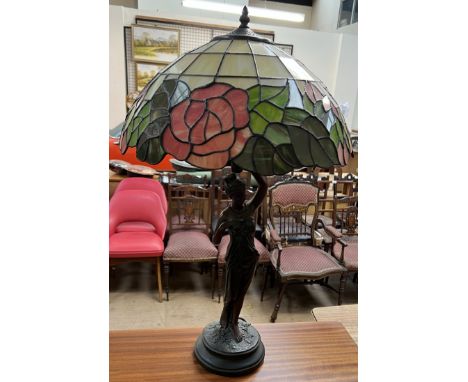 A Tiffany style table lamp, the glass shade with floral and leaf panels, held aloft by a maiden
