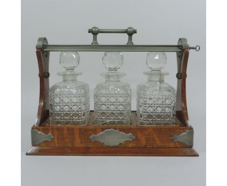 An early 20th century light oak and metal bound tantalus, containing three hobnail cut decanters and stoppers, with a Grinsel