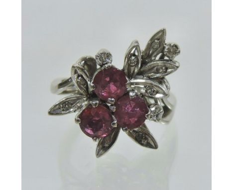 An 18 carat white gold diamond and ruby cluster ring, of asymmetrical design, set with three rubies