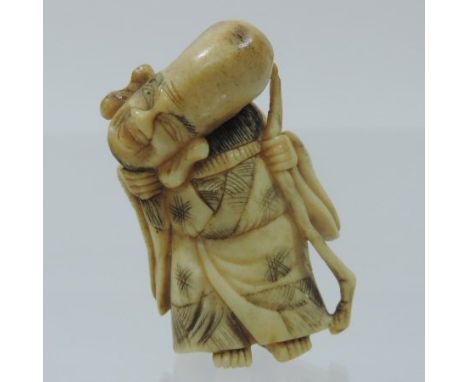 A Japanese carved stag antler netsuke, probably 19th century, in the form of Fukurokuju, pulling his beard and holding a staf