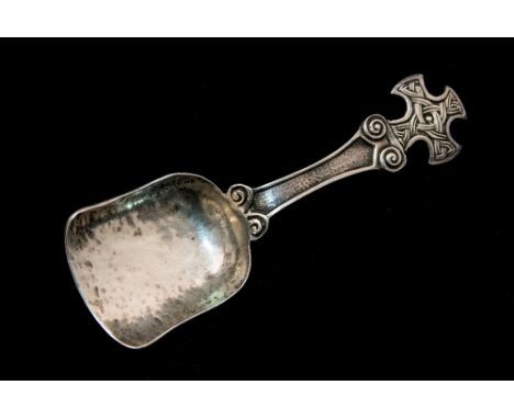 A Scottish Arts and Crafts silver caddy spoon, Iona style, the handle in the form of a Celtic cross, hand hammered shovel bow