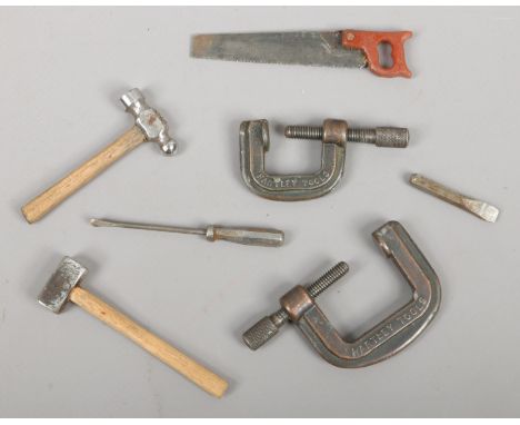 A collection of miniature apprentice tools including wood saw, two hammers, two G clamps and a chisel and a screw driver.