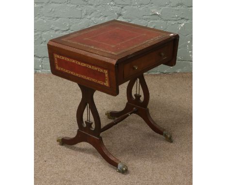 A mahogany dropleaf sofa table with red leather top raised on lyre supports.