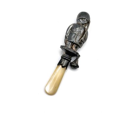 A silver baby's rattle in the shape of a Coldstream Guard in uniform with a mother of pearl handle. Missing a bell, and heavi