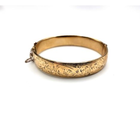 A 9ct yellow gold 1/5 metal core bracelet/ bangle with safety chain. Foliate design on the hinged top half. 22.1gms.