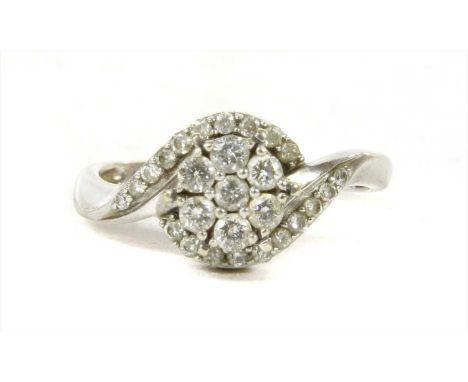 A white gold diamond cluster ring, a brilliant cut diamond daisy cluster head to crossover shoulders, set with a graduated ro