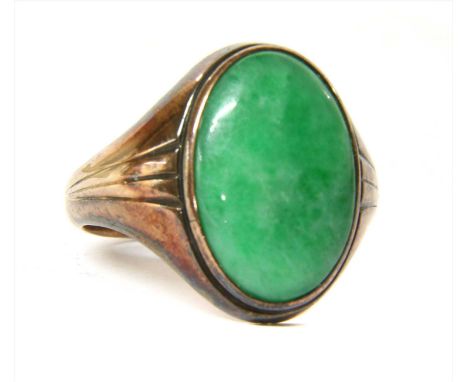 A gold single stone jade ring, an oval jade cabochon, rub set to a plain collet, with grooved tapered shoulders and a plain s