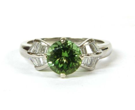 A platinum peridot and diamond ring, a circular mixed cut peridot, claw set, to arched shoulders channel set with two rows of