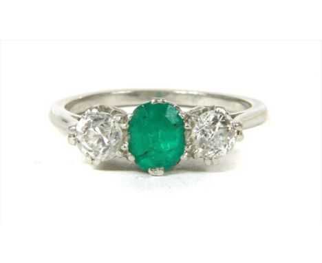 A three stone emerald and diamond ring, with an oval mixed cut emerald, with an old European cut diamond at each side, all cl