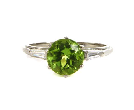 A platinum peridot and diamond three stone ring, a circular mixed cut peridot, claw set with a tapered baguette cut diamond a