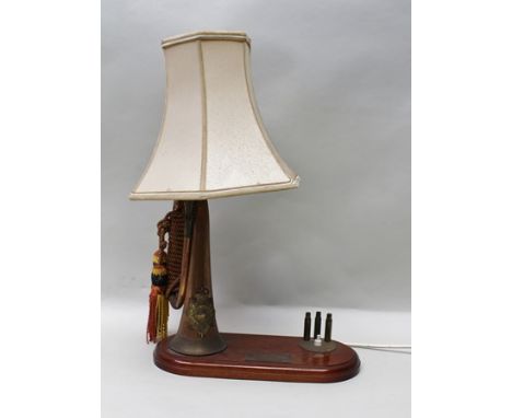 AN INTERESTING AND DECORATIVE TABLE LIGHT formed from a military bugle, supported on an oval wooden mahogany plinth base with