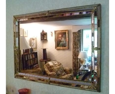 A VENETIAN DESIGN WALL MIRROR with a cushion frame, with decorative brass flower head devices around a central plate, overall