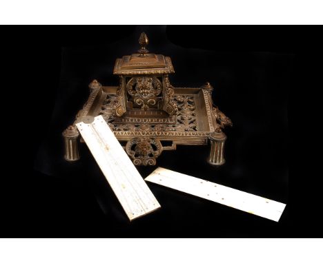 A Victorian brass inkwell,  on pierced mask and pillar base, 19cm wide, together with a Delftware example, two ivory rules an