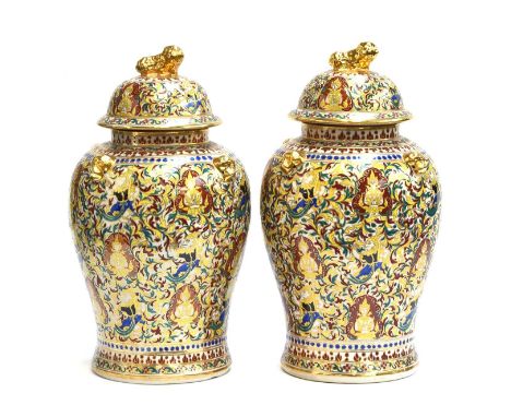 A pair of large decorative ceramic urns and covers, buddhas on a profuse floral ground, heightened in gilt with four lion mas