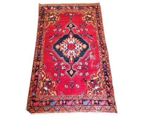 An early 20th century oriental Nomadic hand woven woolpile rug, vivid red ground with central dark blue motif with blue, salm