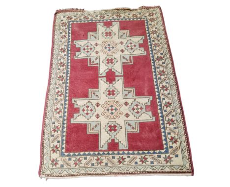 An early 20th century Turkish Kazakh rug on a red ground with blue, cream and pink geometric motifs and borders, 183cm x 127c