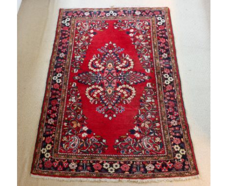 A Persian rug - with a large floral medallion and spandrels on a madder ground, within a blue floral border and light brown f