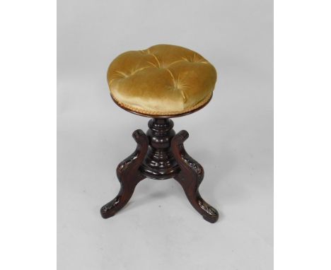 A Victorian mahogany revolving piano stool, with a circular buttoned seat, raised on a turned column and three leaf carved ca