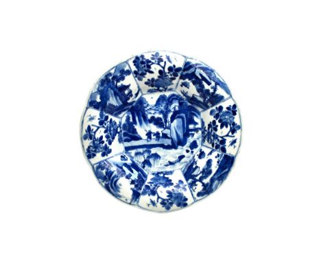A Chinese blue and white small lobed dish, Kangxi, painted in the centre with figures in a mountainous landscape, beneath a p