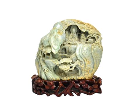 A Chinese jade boulder carving, of pale celadon tone with light brown and cream  inclusions, carved with buddha seated in a g