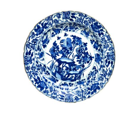 A Chinese blue and white dish, Kangxi, painted in the centre with flowering shrubs and rocks, beneath panelled borders enclos